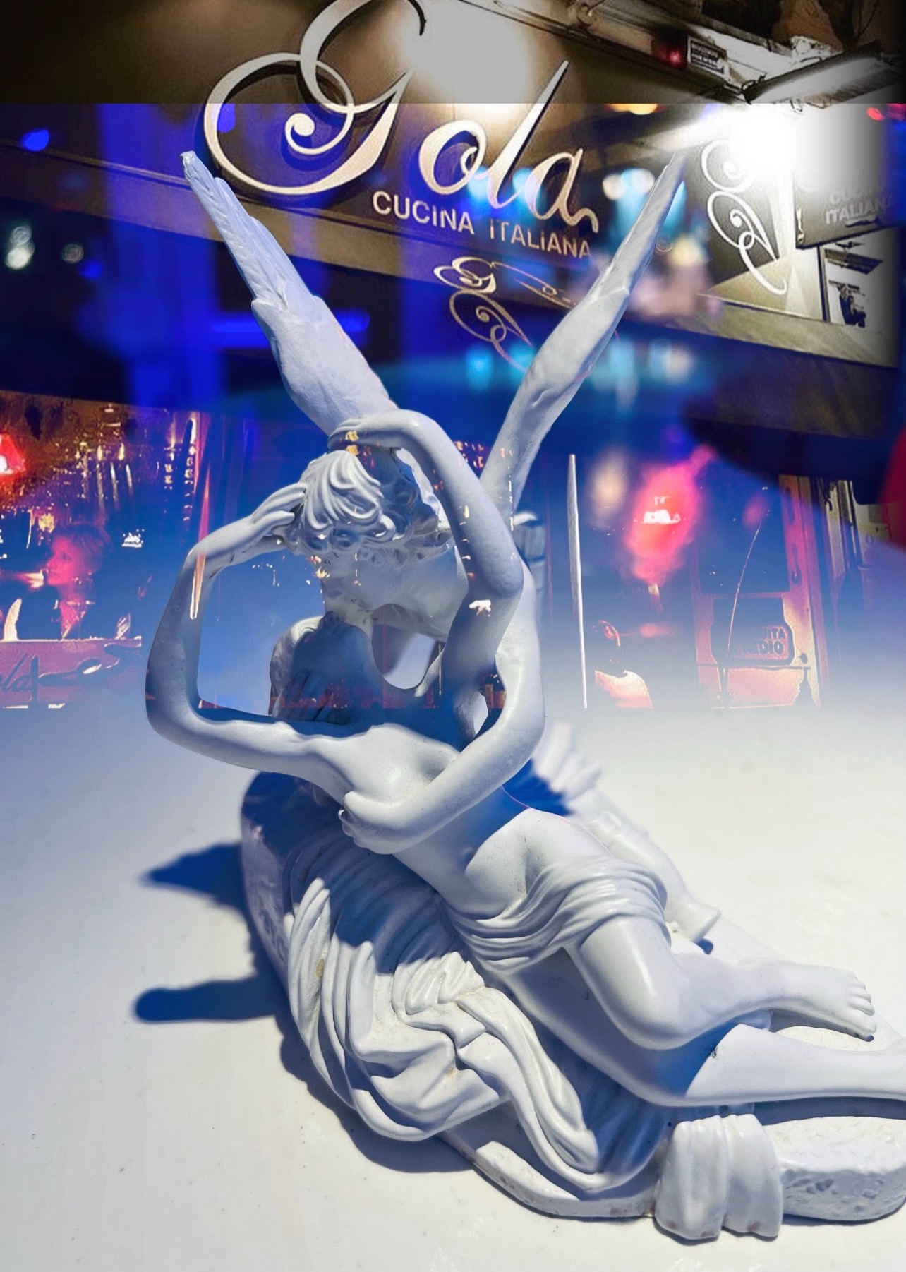 A sculpture of two embracing figures in front of the Gola sign