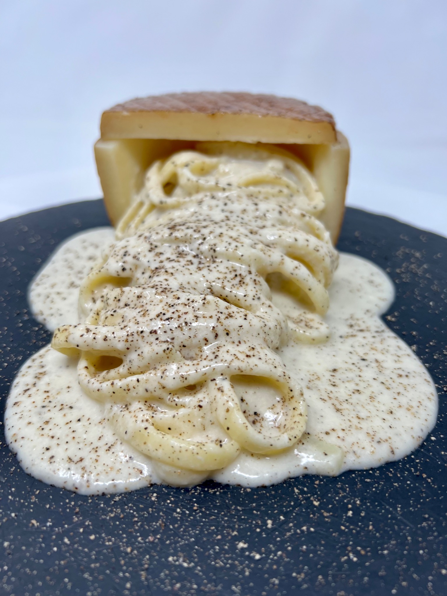 Cacio e pepe pasta served from a hollowed cheese, with black pepper