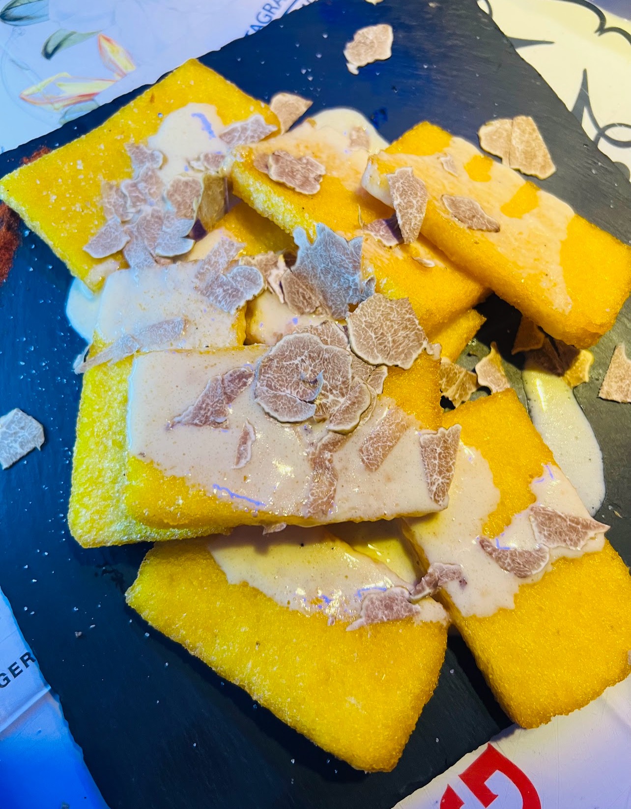 Golden scagliozzi, pieces of fried polenta served on a dark platter