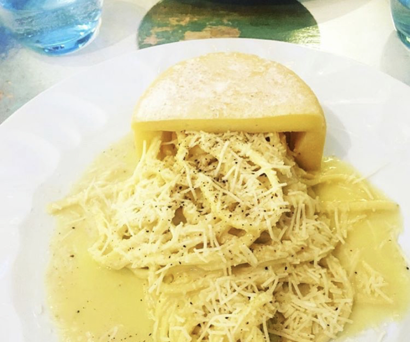 Pasta served from a hollowed cheese wheel with grated cheese and black pepper