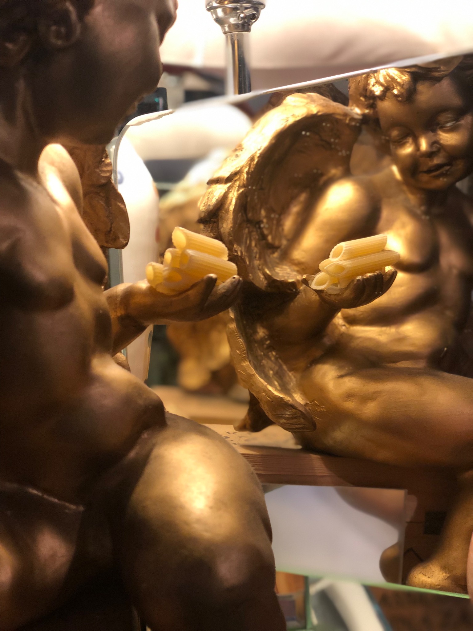 A golden cherub holding penne, reflected in a mirror inside Gola