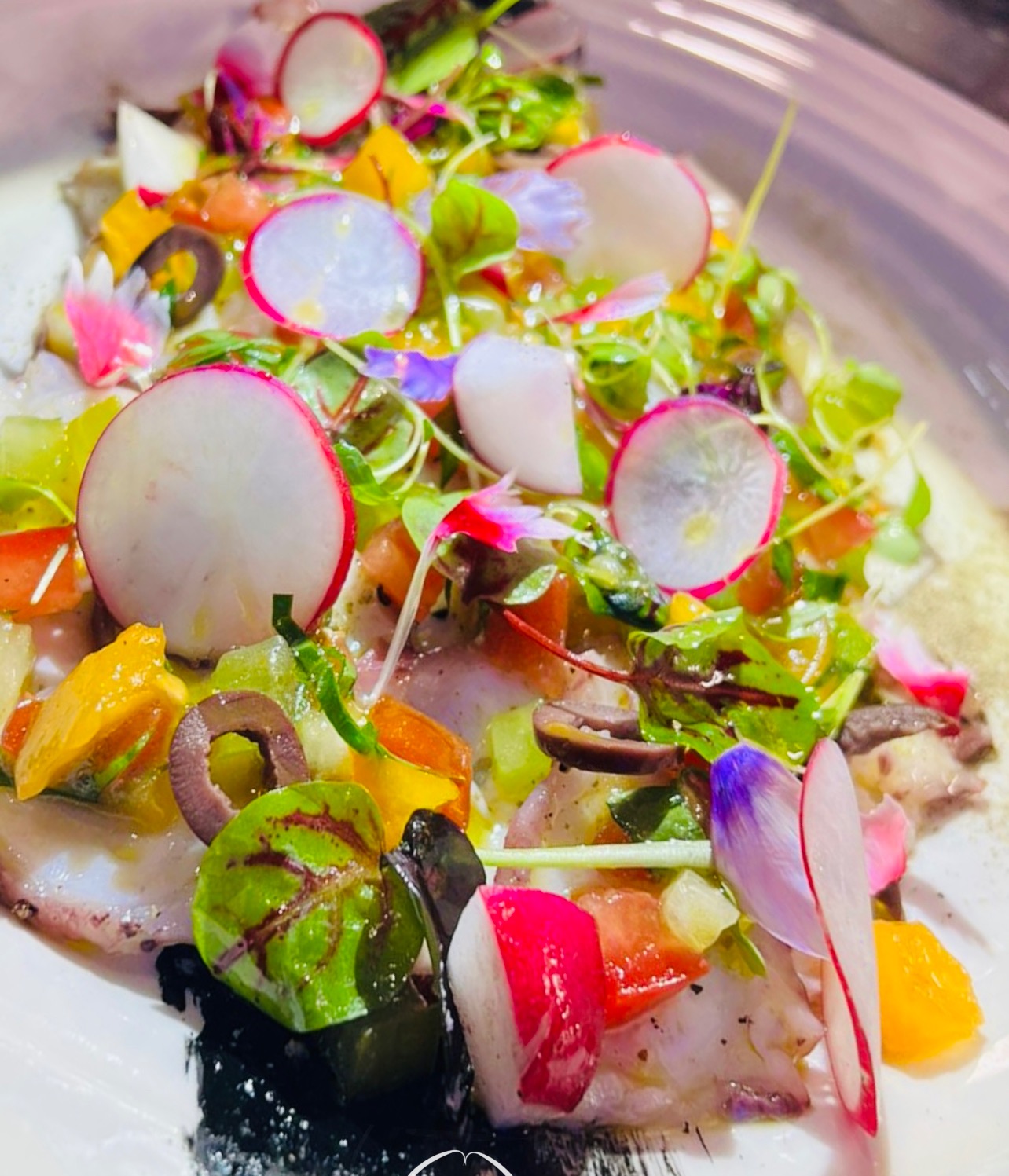 Thin slices arranged on a white plate with radish, olives, herbs and edible flowers