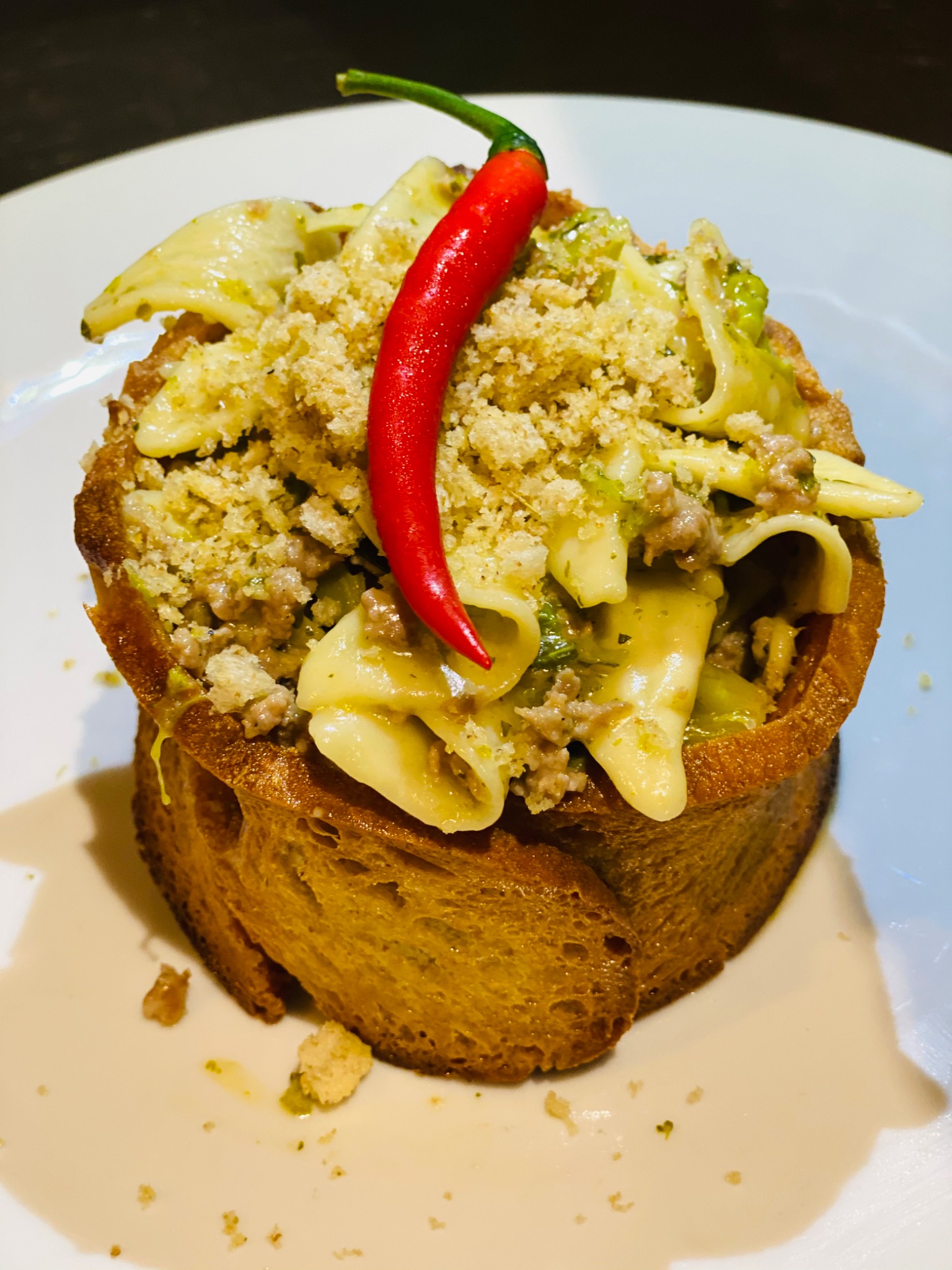 Short pasta in a bread bowl, topped with green sauce, a crumbled garnish and a red chilli