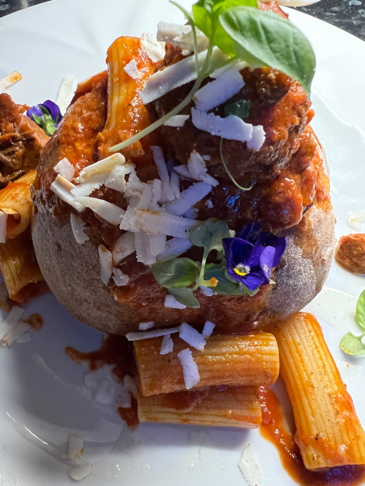 Rigatoni in red sauce with cheese shavings, basil and violet flowers